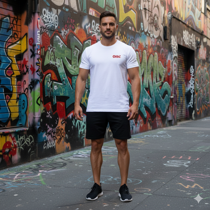 Man wearing a white t-shirt with red text and black shorts standing in front of a graffiti-covered wall.